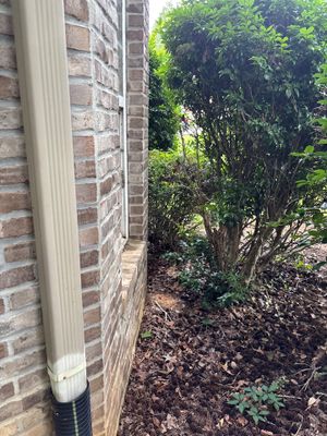 Exterior foundation perimeter showing a white drainage pipe installed along the brick foundation with mulched