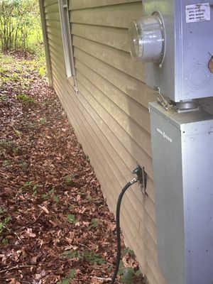 Exterior foundation wall with an installed drain discharge line and catch basin or drainage hardware visible at ground