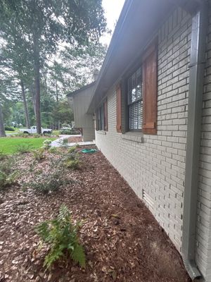 Exterior view of a brick foundation with landscaped yard showing no visible repair work, drainage hardware, or
