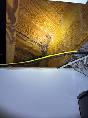 Interior crawlspace or basement showing exposed wooden beams and joists with a yellow drainage pipe or conduit