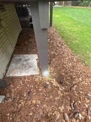 Exterior yard drainage work showing mulch/wood chip base material laid around the foundation perimeter with a concrete