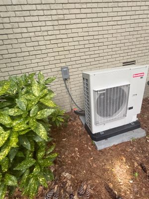 Exterior HVAC unit installed against brick foundation with completed yard drainage system visible, including mulched
