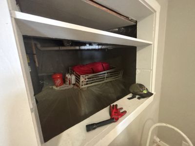 Interior storage area or crawlspace showing red bins, equipment, and work gloves staged before foundation repair work