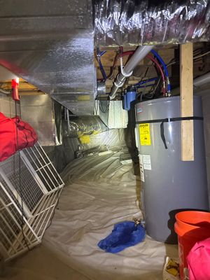 A crawlspace is being waterproofed with a plastic vapor barrier being installed on the floor, and an interior drainage