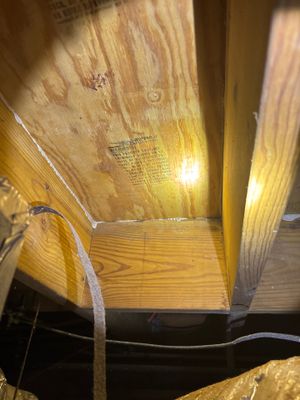 Interior drainage system installation in progress showing wooden framing, white drainage pipe, and staging materials in