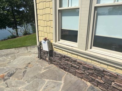 Exterior view of a residential foundation showing a stone veneer base and large windows with no visible repair work,