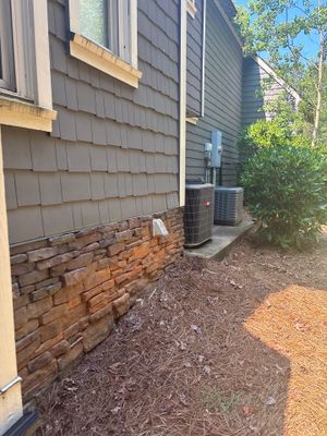 Exterior foundation area showing exposed brick foundation with mulch ground cover and a yard drainage catch basin or