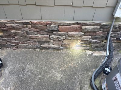 An exterior foundation area showing deteriorated stone/brick veneer with visible moisture damage and moss growth, with