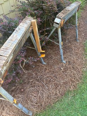 Exterior yard drainage installation in progress with two ladder-supported drainage channels or gutters positioned in a