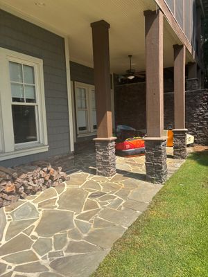 Completed exterior patio installation with decorative flagstone concrete flatwork, drainage rock bed, and finished