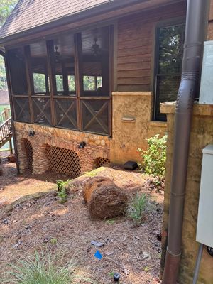 Exterior foundation area showing exposed brick/stone foundation with decorative wooden lower level, landscaping with