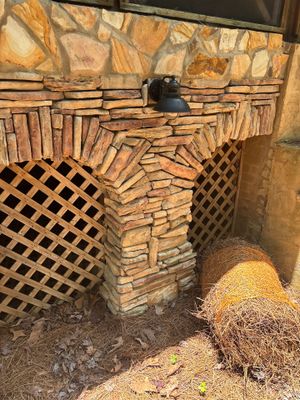 Foundation wall with exposed brick/stone construction and deteriorating mortar joints; black lattice venting visible
