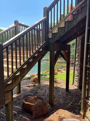 Exterior yard drainage installation in progress beneath a wooden deck with visible excavation, gravel base, and