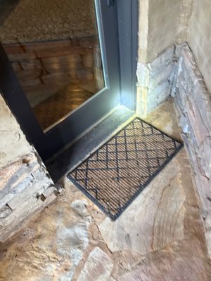 A black metal drain grate installed at a foundation entry point with visible excavation and exposed concrete foundation