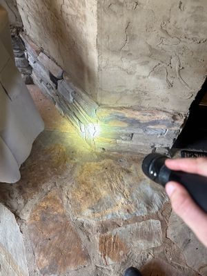 A worker is actively applying a yellow waterproofing membrane or coating to an interior foundation wall corner where