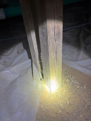 An interior drainage system installation at a foundation with a bright LED work light illuminating a perimeter drainage