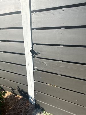 A white post and horizontal gray wooden fence boards with black horizontal straps, showing structural framing before