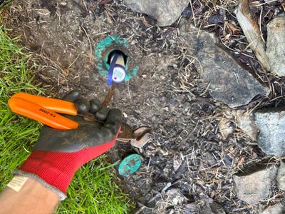 An exterior catch basin or yard drainage system being installed in soil with a blue-marked opening, measurement tools