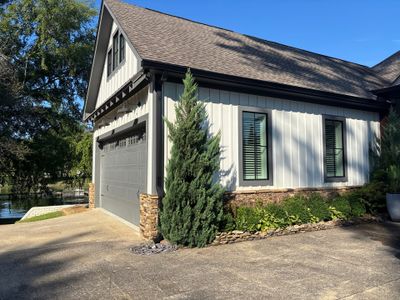 A newly constructed modern farmhouse with white vertical siding, black trim, dark roof, stone foundation accents, and