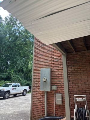 A brick foundation wall with exterior electrical fixtures and a metal roof overhang, showing the existing structure