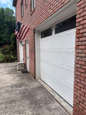 A residential brick garage with a white sectional garage door and an American flag, showing no visible foundation