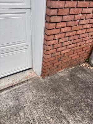 A white garage door frame against a red brick wall with a concrete driveway floor showing no visible repair work or