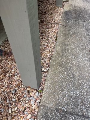 Exterior foundation drainage work in progress showing a concrete pad adjacent to gravel and decorative stone