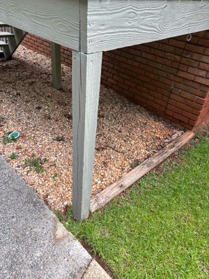Exterior foundation area showing installed yard drainage work with gravel base and wooden timber edging along a brick