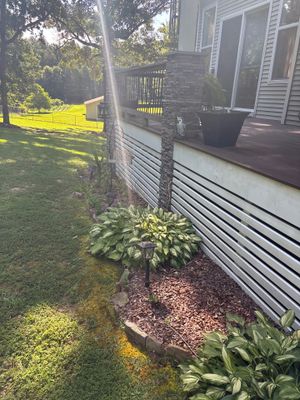 Exterior view of a house foundation with a lawn, deck, and landscaping showing no visible repair work or drainage