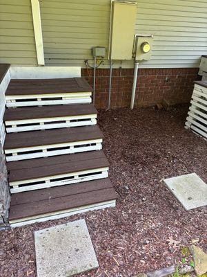 A crawl space foundation area with wooden deck stairs, gravel flooring, and visible white PVC pipe or encapsulation