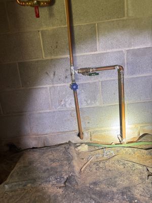 Interior foundation drainage system being installed with copper piping and blue shut-off valve against a block