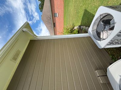 A completed exterior deck or porch with metal decking, gutters, downspout, and HVAC unit visible against a brick house
