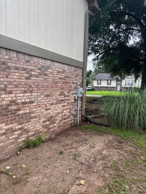 Exterior foundation area showing bare soil, brick foundation wall, white vinyl siding, and ornamental grasses