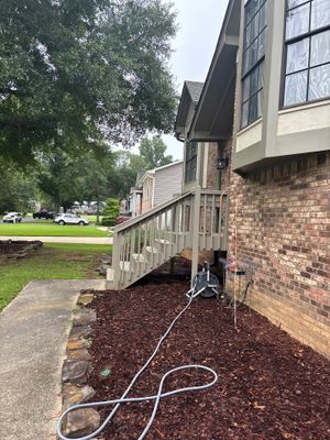 Exterior yard drainage installation in progress with a gray discharge hose laid across freshly mulched ground beneath a