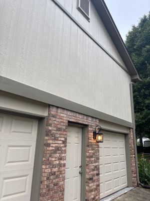 A completed garage exterior showing new white fiber cement siding, brick foundation pillars, white garage doors, and a