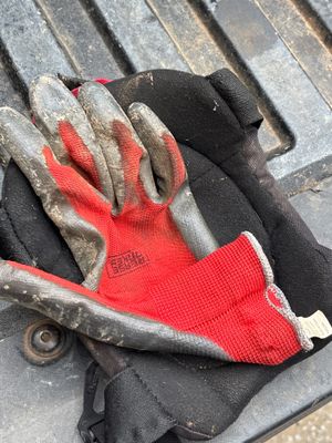 Work gloves with red palms and gray reinforced fingers resting on a dark roofing material or surface, indicating active