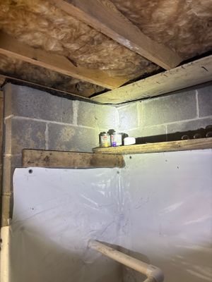 A crawlspace during active waterproofing work, showing white plastic vapor barrier installation on the floor, exposed