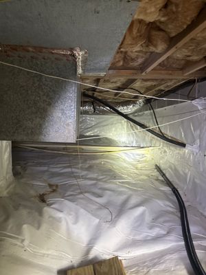 A crawlspace undergoing encapsulation with white plastic vapor barrier installed on the floor, exposed joists and