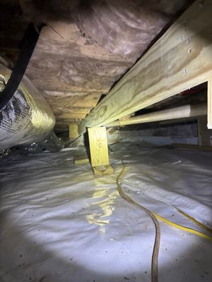 Active crawlspace encapsulation installation with vapor barrier being laid, wooden support posts, and yellow electrical