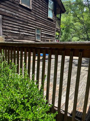 A wooden deck with railings attached to a dark-sided house with landscaping vegetation visible, showing the exterior