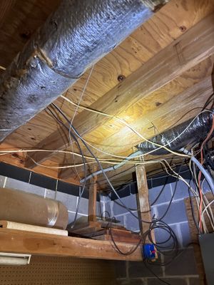 Interior crawlspace showing drainage pipe installation with flexible ducting and wiring routed along wooden beams and
