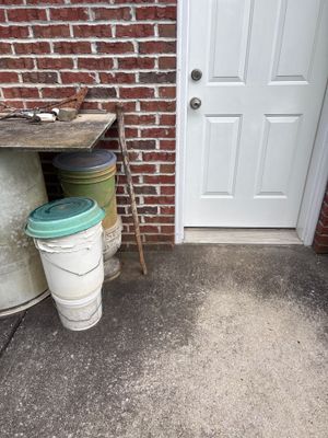 Exterior view of a brick foundation with white door and stacked buckets, showing no visible repair work or drainage