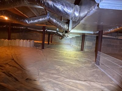 A crawlspace encapsulation installation in progress showing plastic sheeting being laid over the floor with support