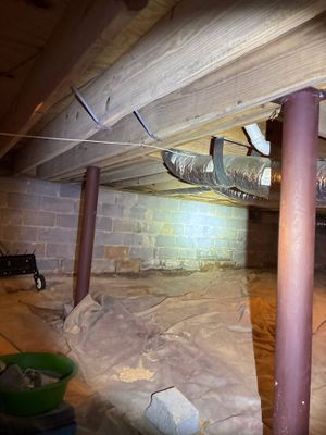 A crawl space under active waterproofing and encapsulation work, with plastic sheeting being installed over the floor