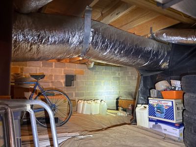 A crawlspace undergoing encapsulation work with a flexible duct system installed and drainage/storage materials visible