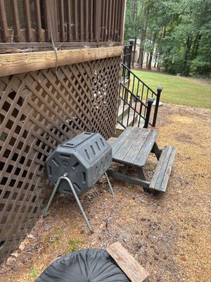 A portable sump pump and collection basin are staged in a yard near a lattice foundation wall during drainage system