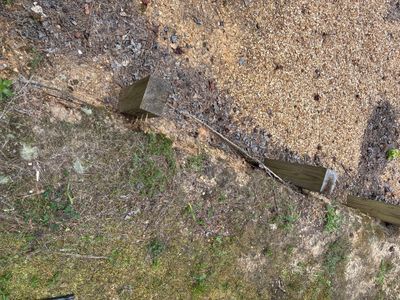Exterior drainage system installation showing a pipe or channel being laid in excavated ground with visible soil and