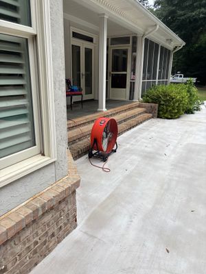 A residential home exterior showing a patio area with brick foundation, new concrete flatwork, and landscaping, with no
