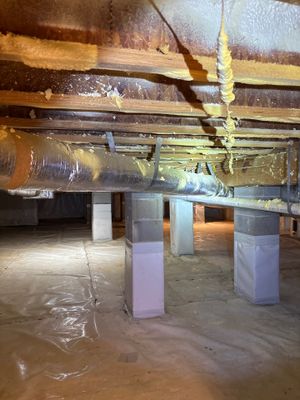 A crawl space is being encapsulated and prepared for drainage work, with plastic sheeting laid on the floor and support