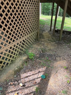 Exterior ground-level view showing a drainage trench or channel with rocks and gravel along the foundation perimeter,
